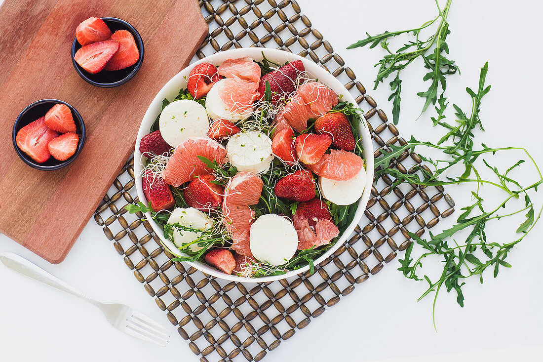 Top view of bowls with strawberry, grapefruit and rocket salad on table served on kitchen boards