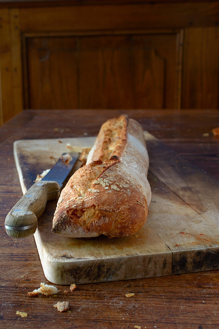 Baguette on a wooden board with a bread knife on a rustic wooden table