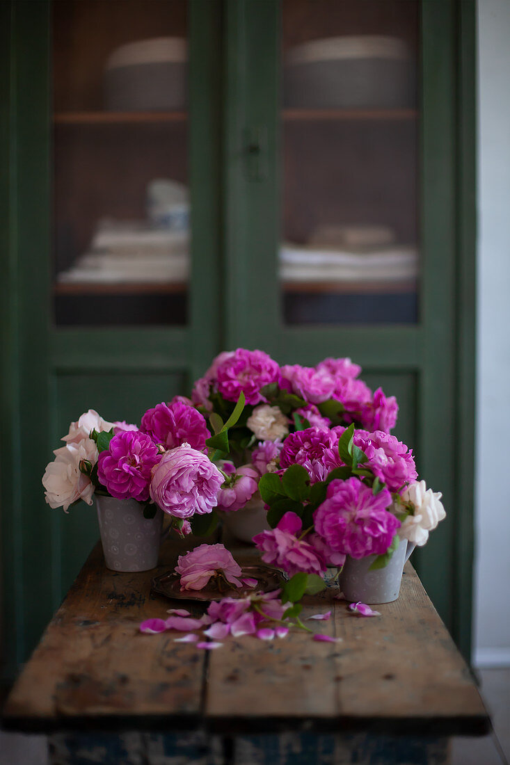 Pinkfarbene und weiße Rosen im Metallgefäßen auf Holztisch