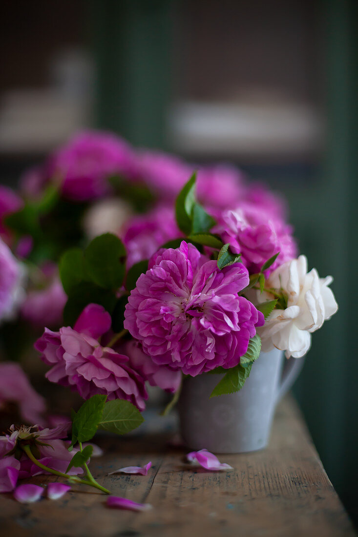 Pinkfarbene und weiße Rosen im Metallgefäß auf Holztisch