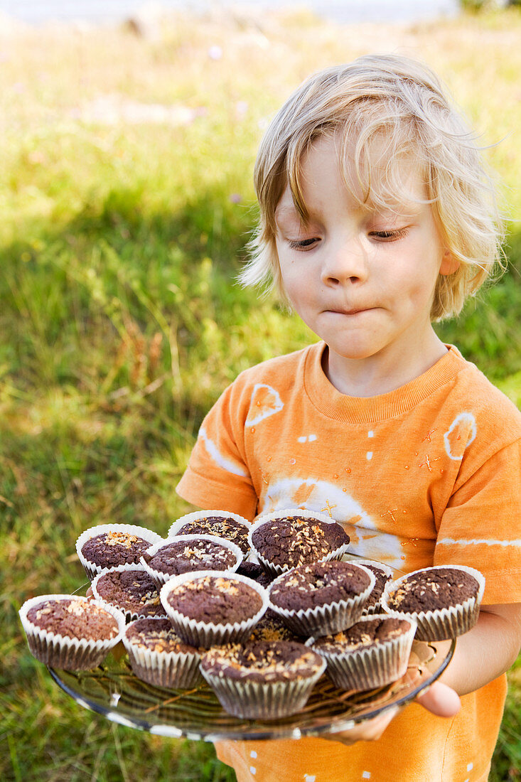 Kleiner Junge mit Schokoladenmuffins auf Glasteller