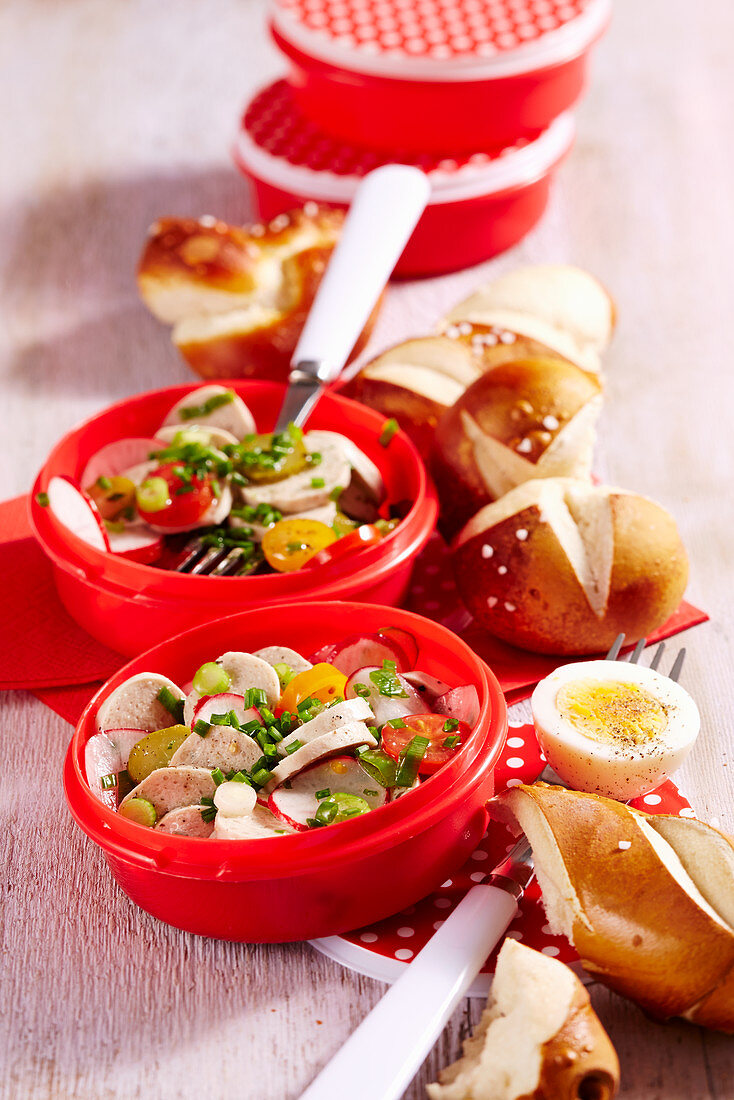 White sausage salad with lye bread rolls in plastic containers to take away