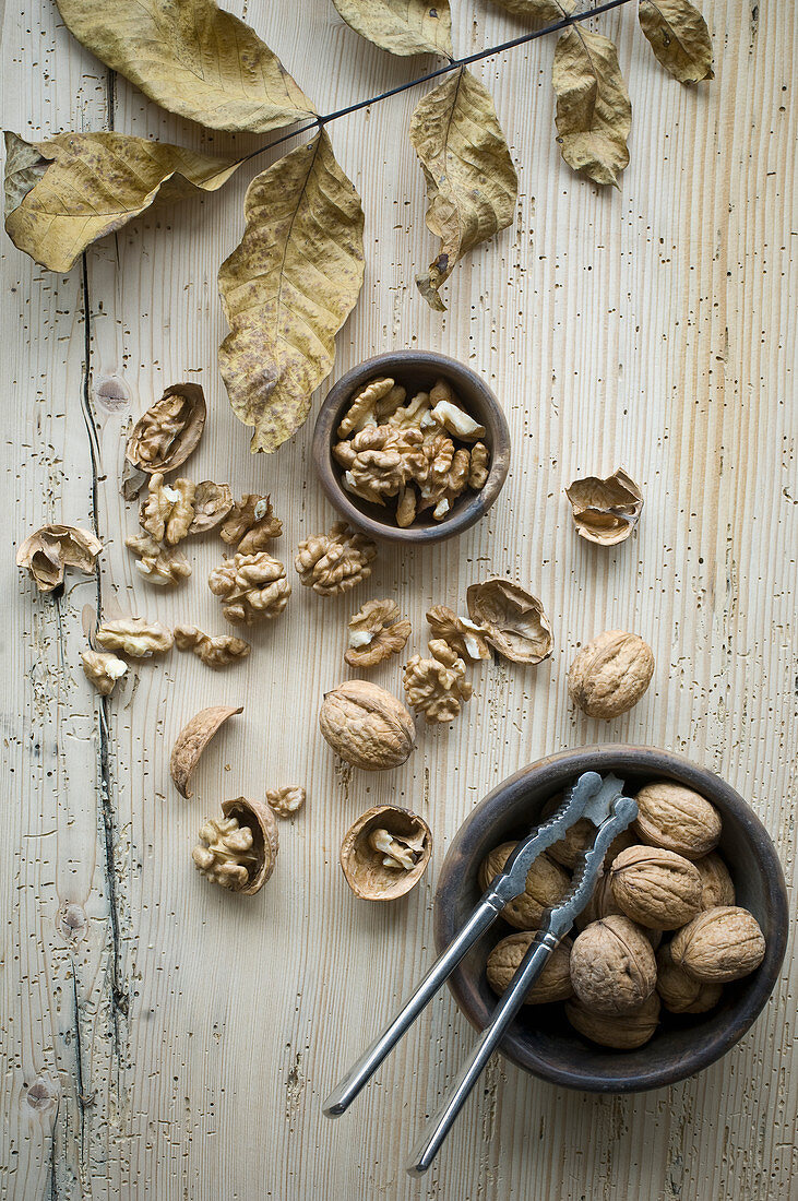 Organic walnuts, whole and cracked, in a bowl with a nut cracker on a rustic wooden surface