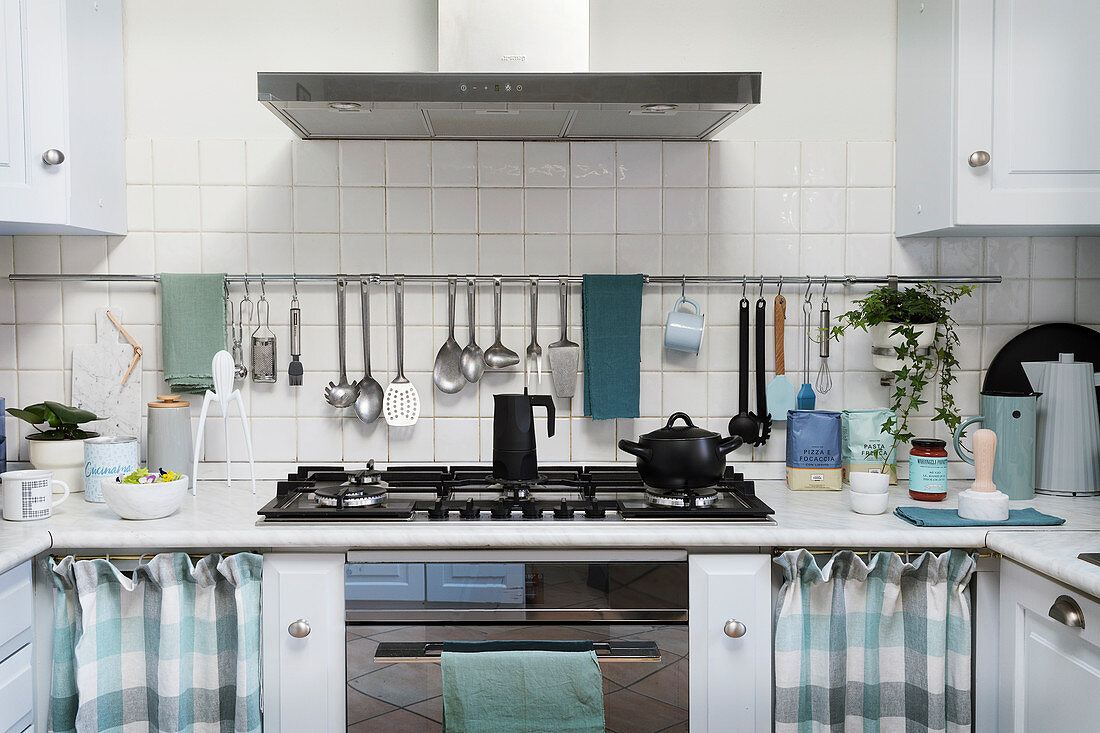 Utensils hung from rod on white-tiled wall above kitchen counter