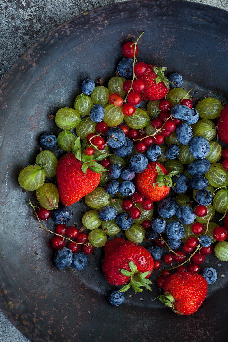 An antique collander filled with strawberries, blueberries, red currants and gooseberries