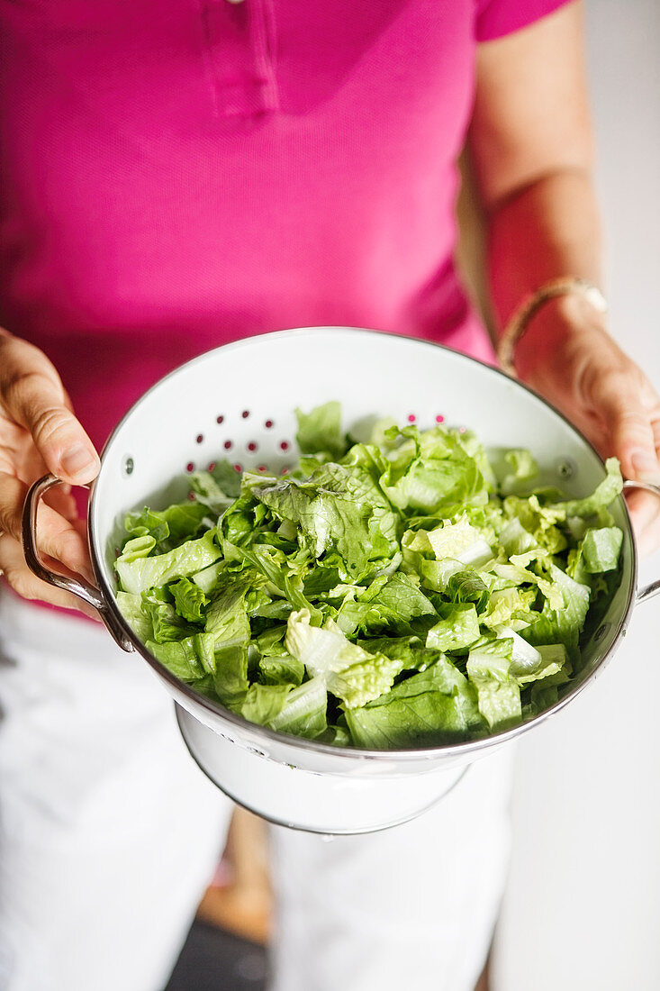 Frau hält Küchensieb mit gewaschenem grünem Salat