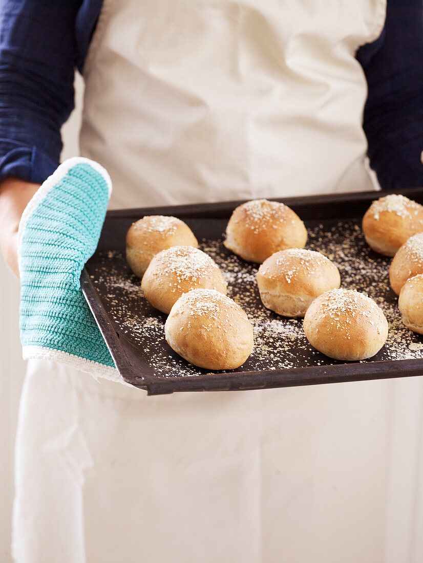 Frau hält Backblech mit Brötchen