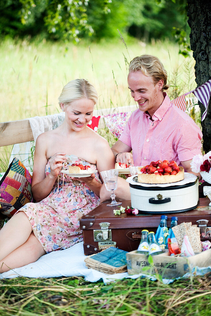 A couple eating strawberry tarts at a picnic
