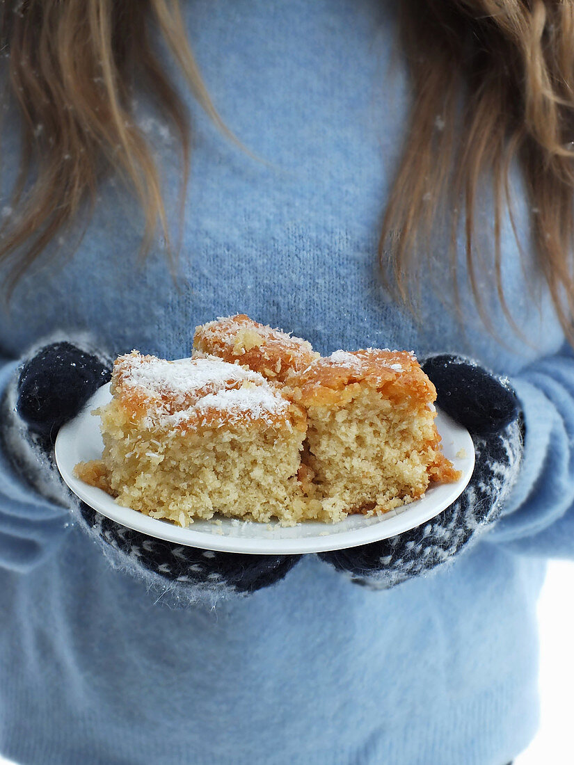 A woman wearing gloves holding a plate of coconut cake