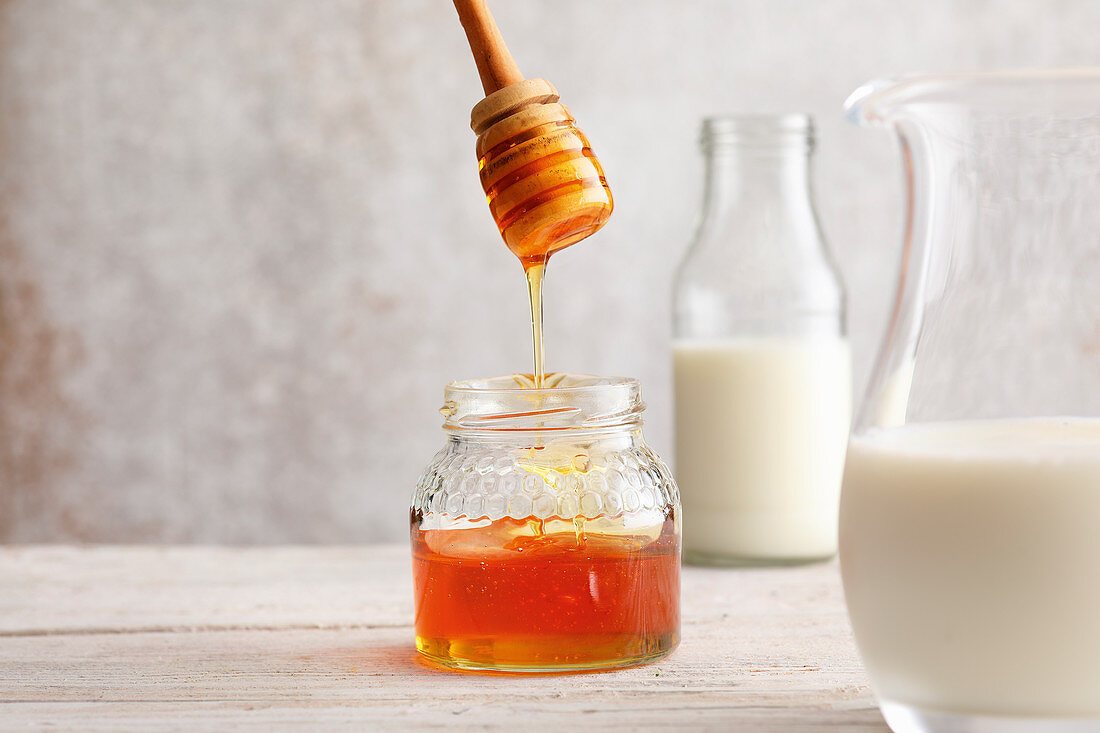 Honig tropft von Löffel in Glas, daneben Milch