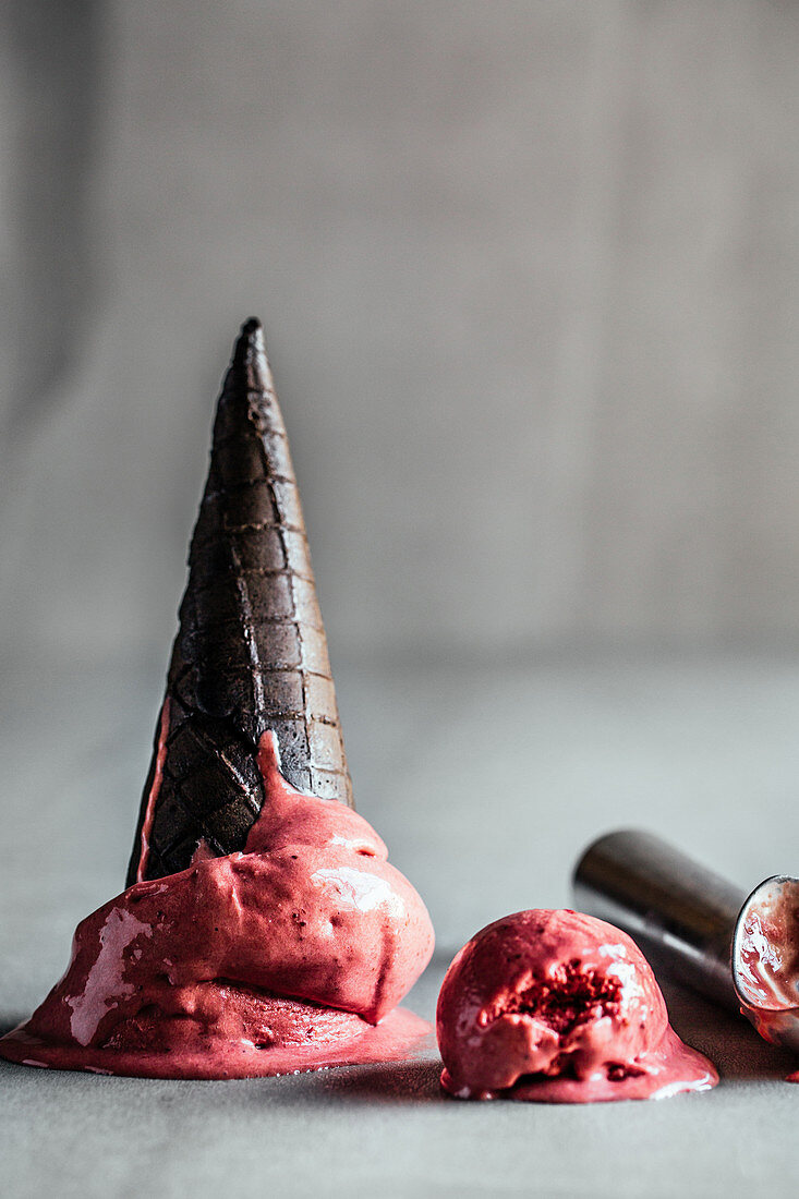 Schmelzendes Erdbeer-Lakritz-Eis mit schwarzer Eistüte