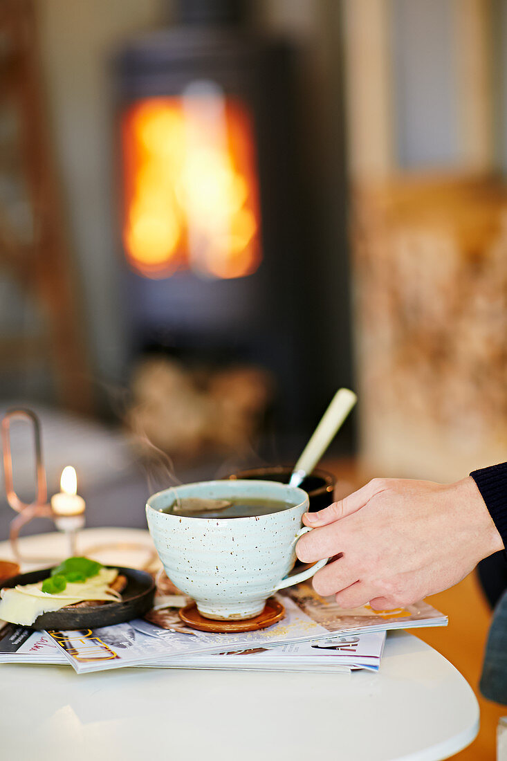 Hand mit Tasse Tee vor dem Kamin