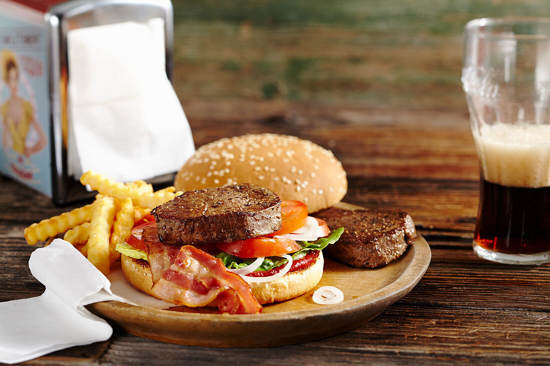 A burger with fried fillet steaks, bacon, ketchup, french fries and cola