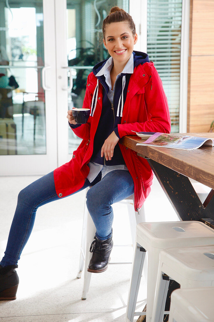 A young woman with a cup of coffee wearing jeans, a hoodie and a short parka