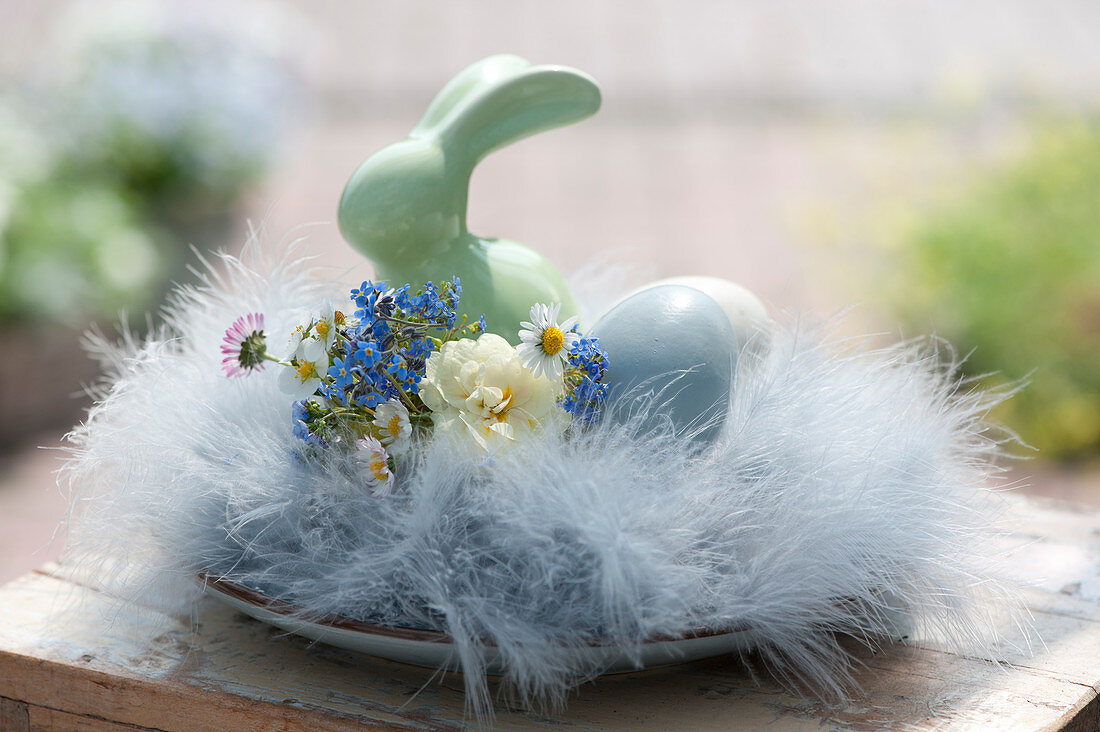 Small Easter nest made of feathers with a bouquet of daffodils, forget-me-nots and daisies