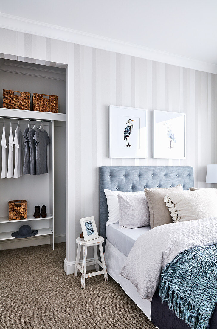 Double bed with button-tufted headboard against striped wallpaper and view into walk-in wardrobe