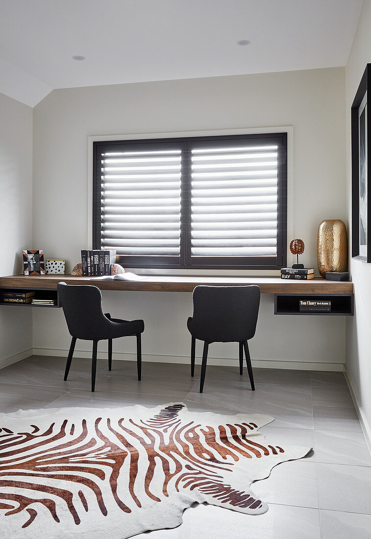 Floating wooden desk, black chairs and zebra-skin rug in study