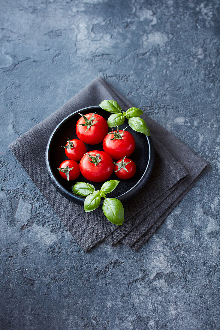 Tomaten in zwei Größen und Basilikumblätter