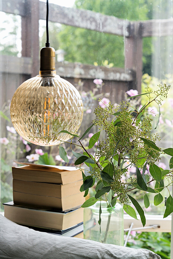 Spherical lamp with structured glass lampshade and vase of leafy branches in front of window