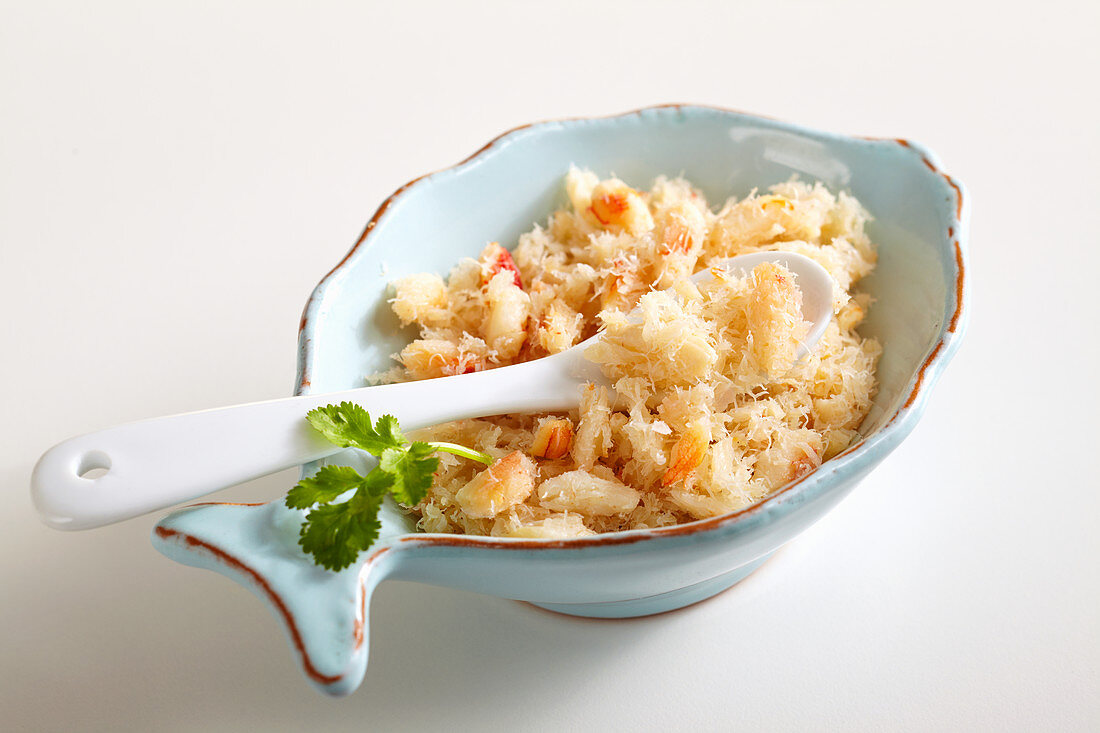 Shredded crab meat in a small bowl with a spoon and coriander leaves