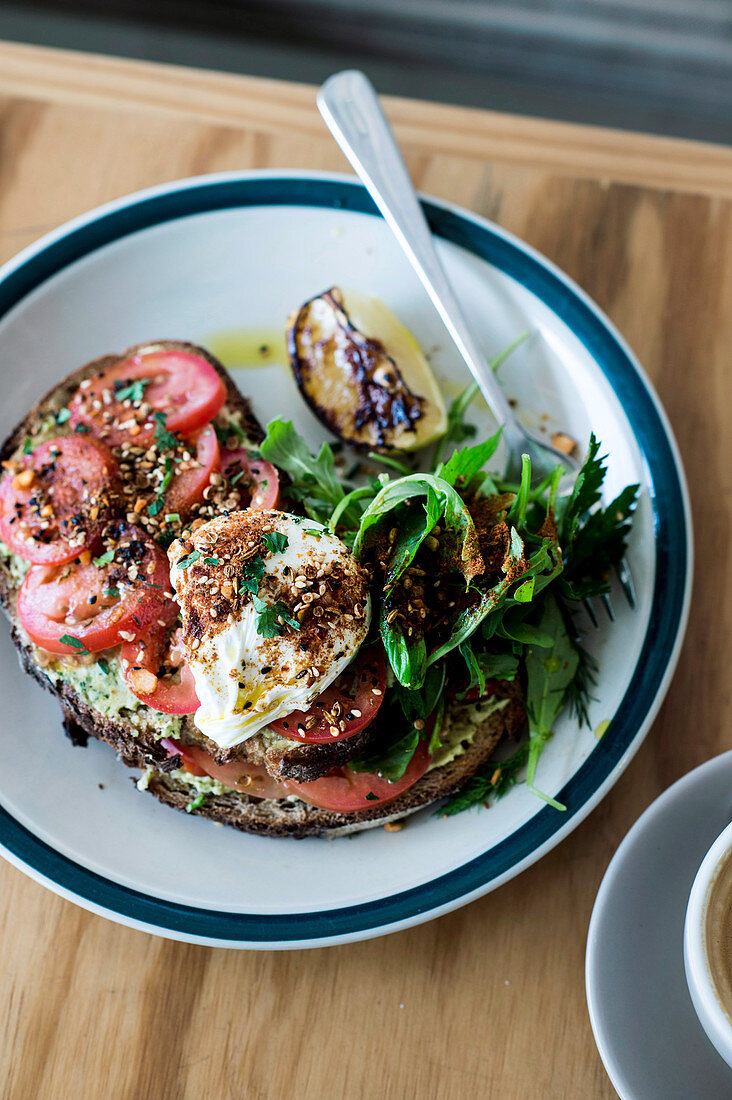 Toasted bread with a poached egg, slices of tomato and avocado puree