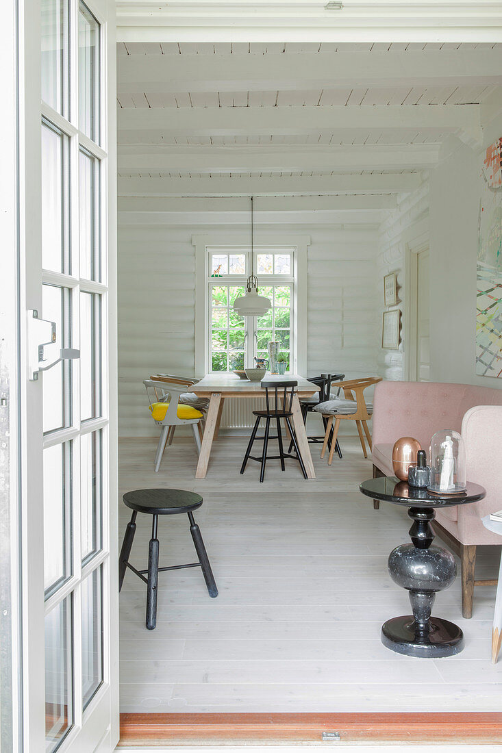 Pink sofa, side table and dining area in background in white-painted log cabin