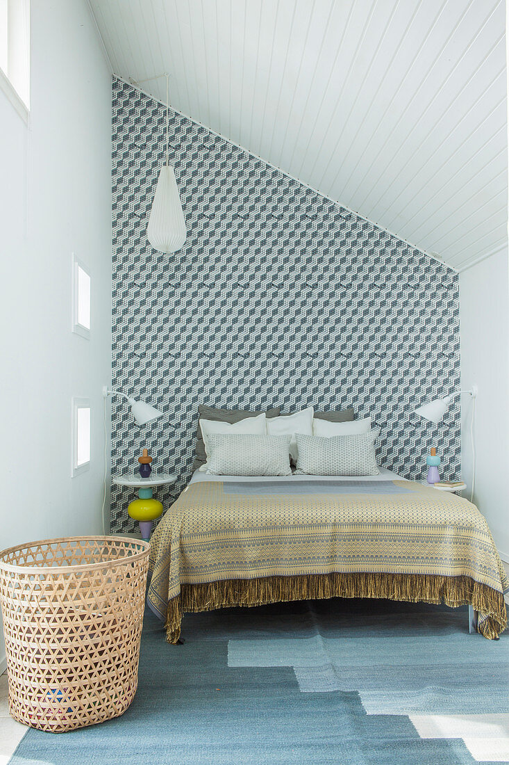 Doppelbett vor Wand mit Tapete im Schlafzimmer mit Dachschräge
