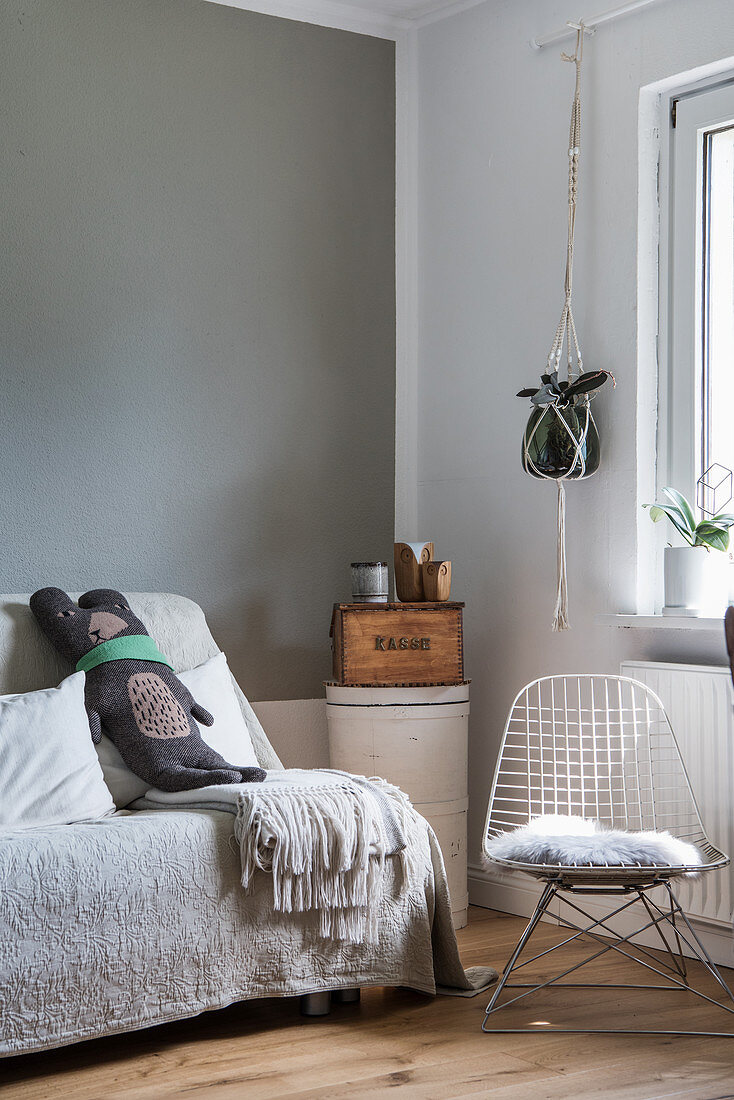 Designer-Drahtstuhl und Sofa mit Überwurf in grau-weißer Zimmerecke