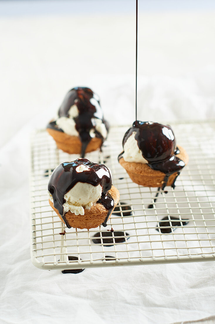 Schokoladensauce fließt auf Mini-Mandelmuffins mit Vanilleiskugel