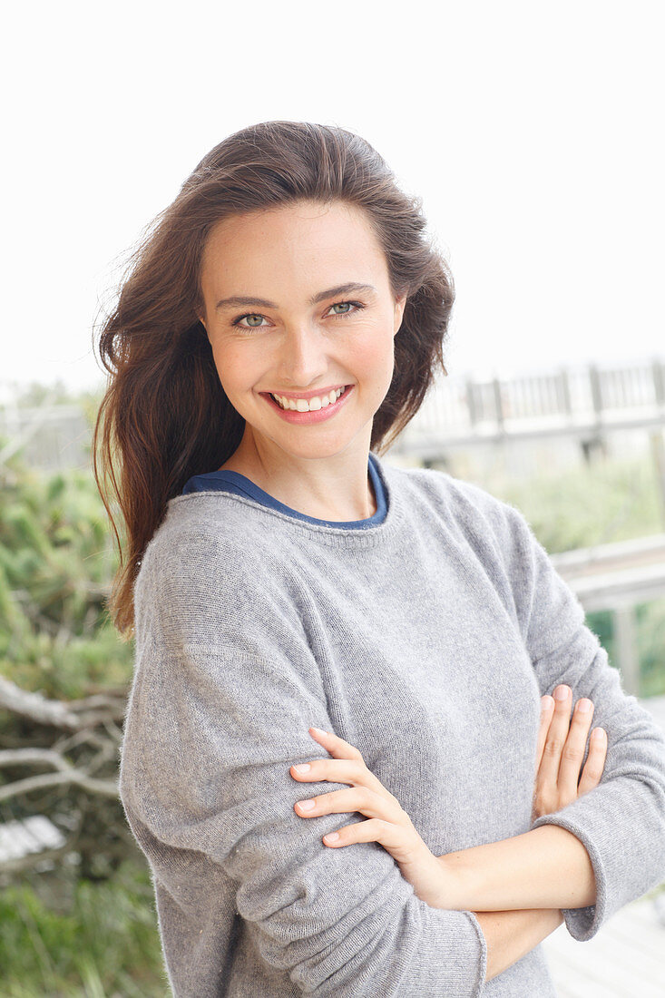 A young brunette woman wearing a grey woollen jumper with an under shirt