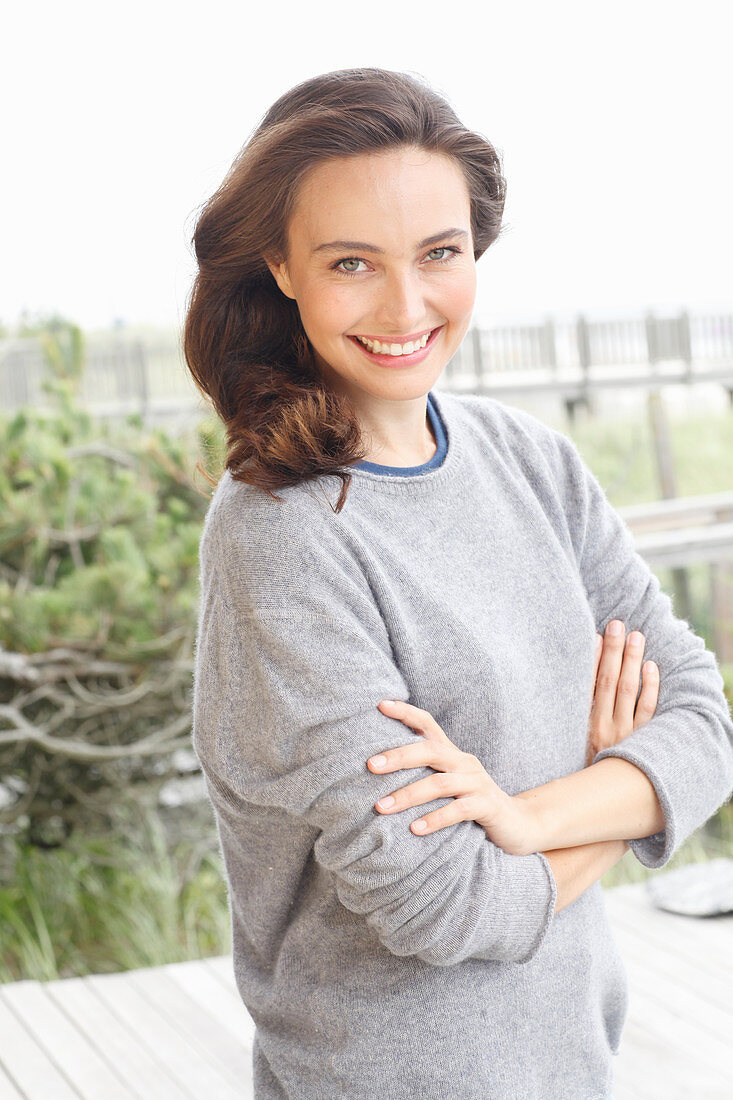A young brunette woman wearing a grey woollen jumper with an under shirt