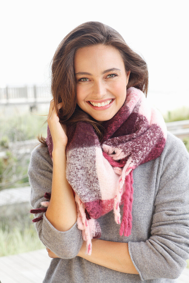 A young brunette woman wearing a grey woollen jumper and a thick scarf