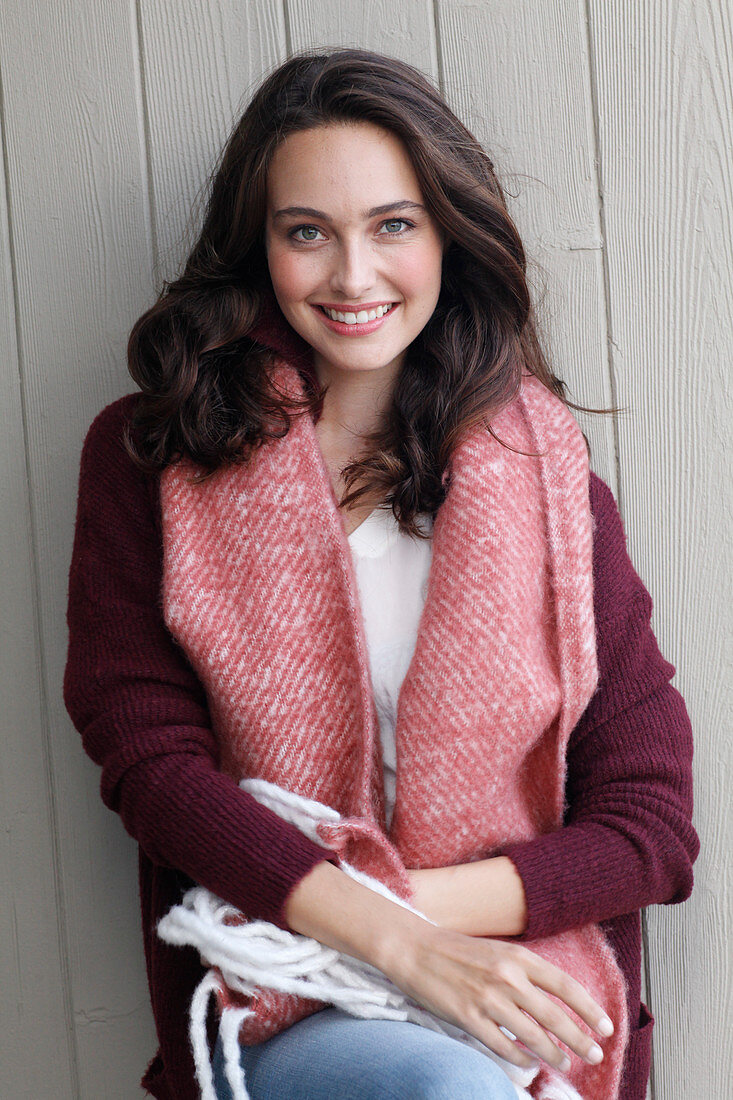 A young brunette woman wearing a wine-red cardigan with a salmon pink woollen shawl