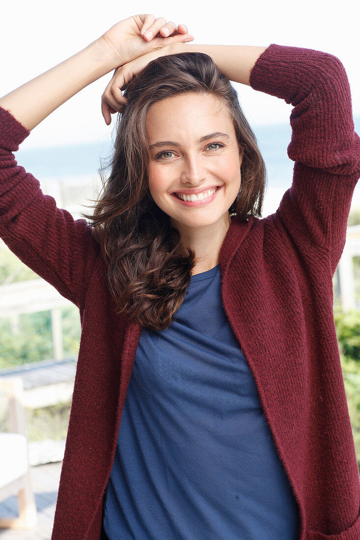 Junge brünette Frau in blauem Shirt und weinroter Strickjacke