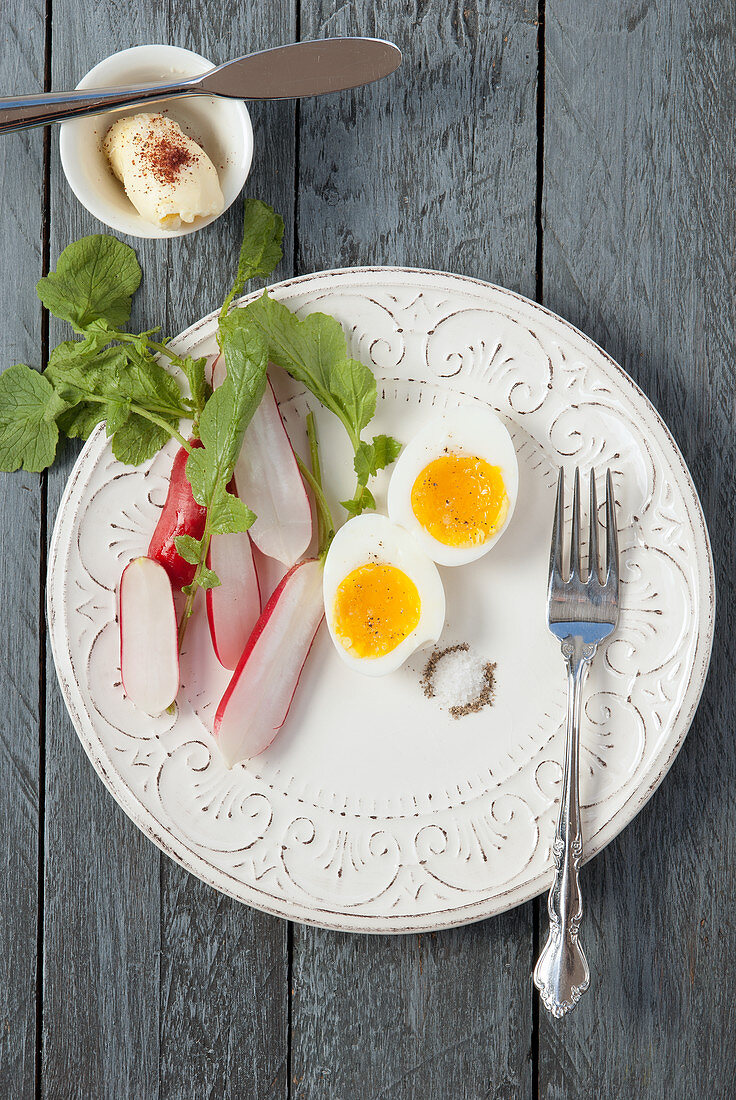 Weichgekochtes Ei mit Radieschen, Salz und Pfeffer, daneben Butter