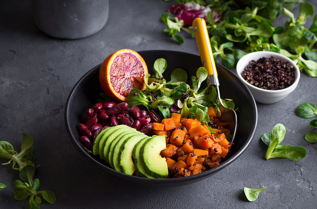 Quinoa salad in bowl with avocado, sweet potato, beans, herbs, orange on concrete rustic background