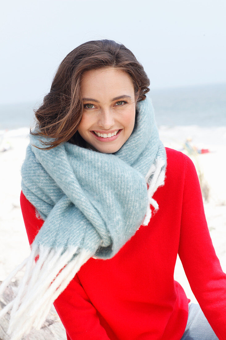 A young brunette woman wearing a red jumper with a thick woollen shawl