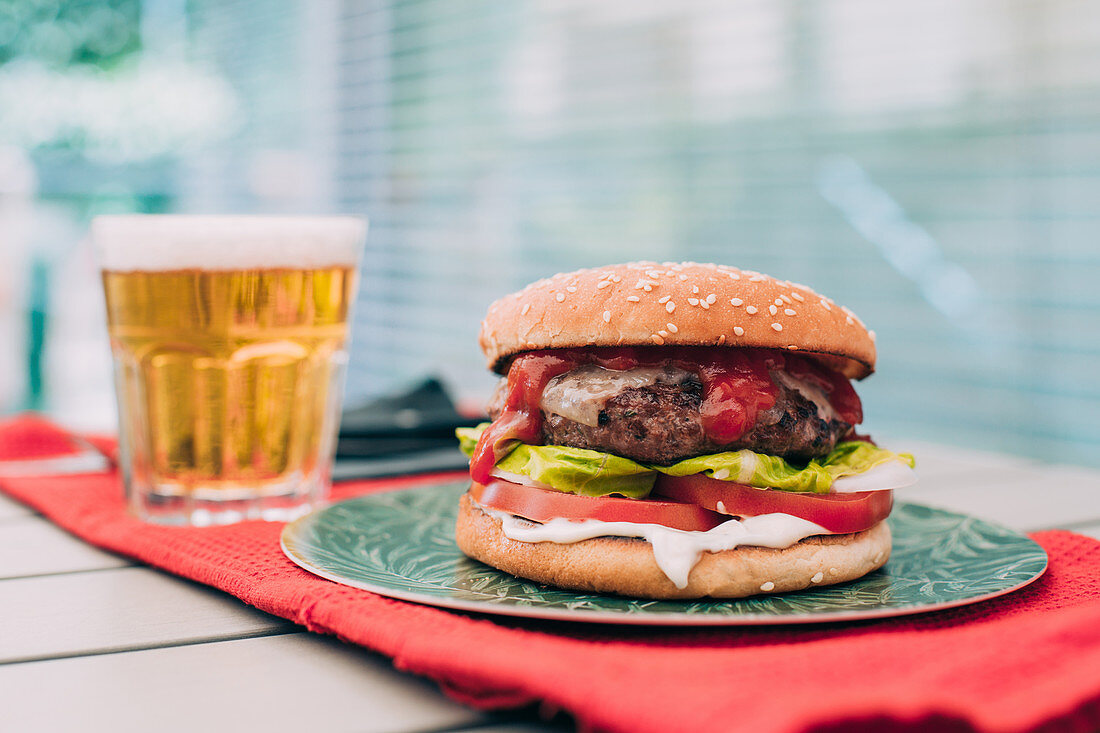 Hausgemachter Cheeseburger mit Tomate und Salat dazu ein Glas Bier