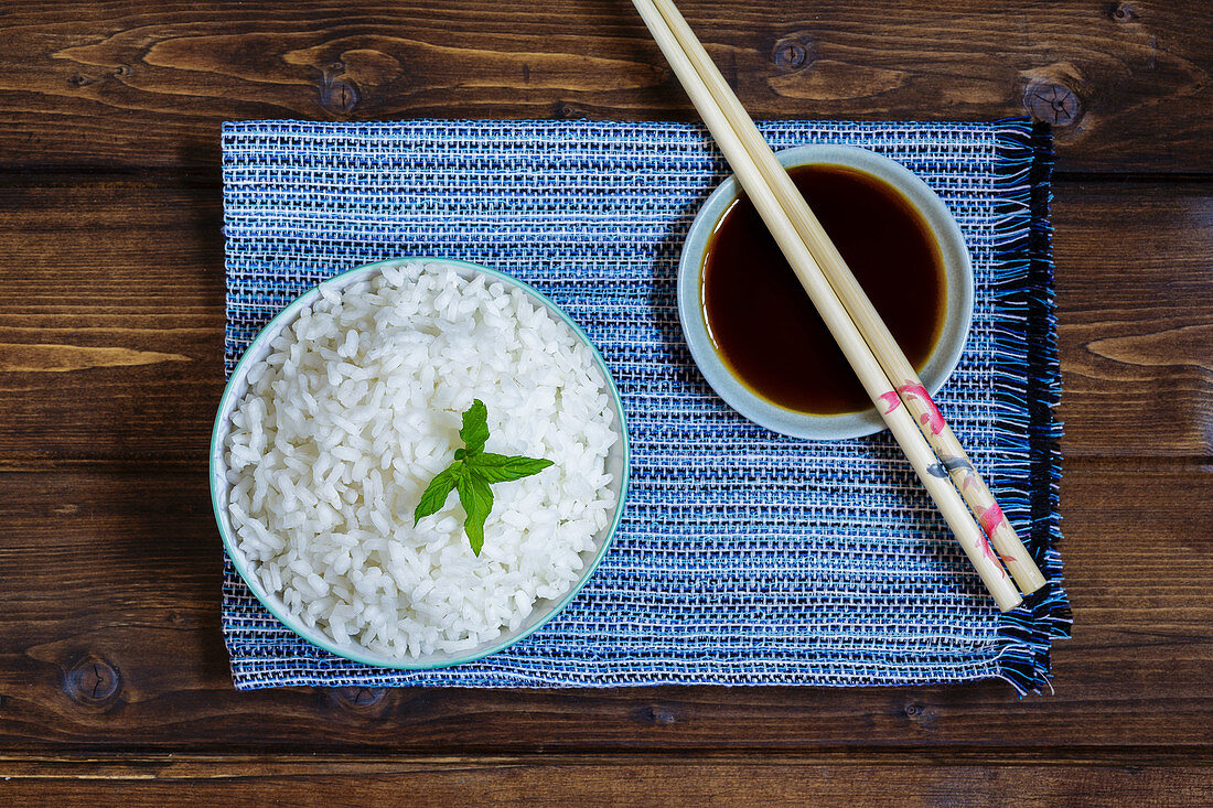 Cooked jasmine rice in a bowl with chopsticks and soy sauce