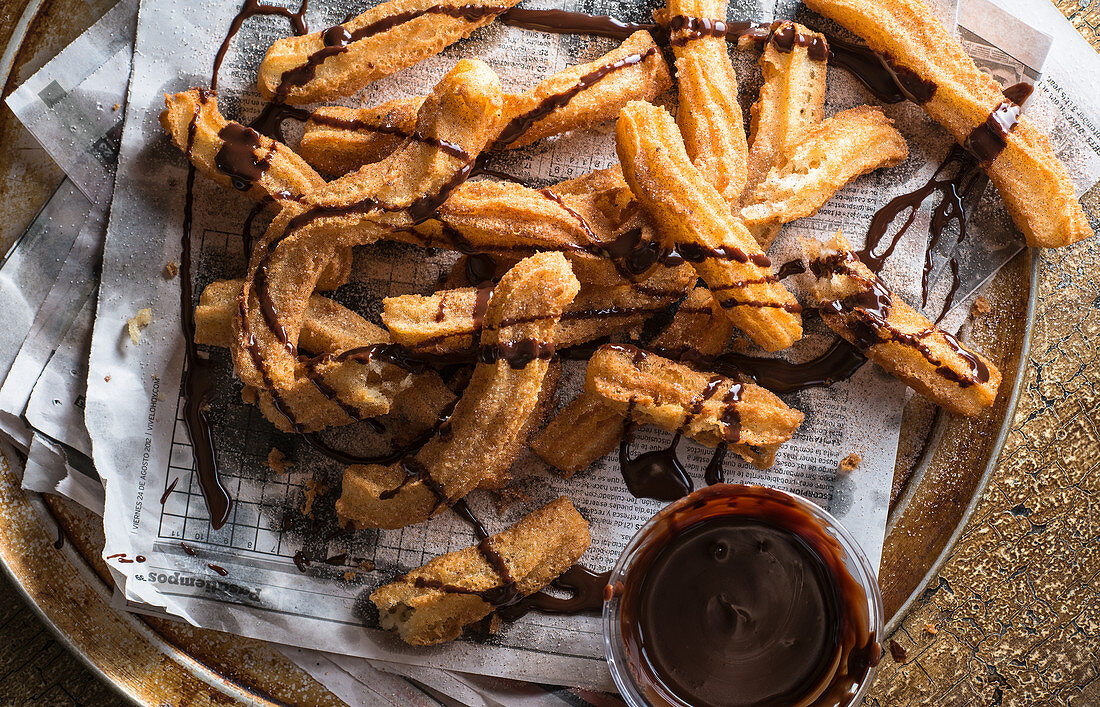 Pile of churros on spanish language newspaper drizzled with chocolate sauce