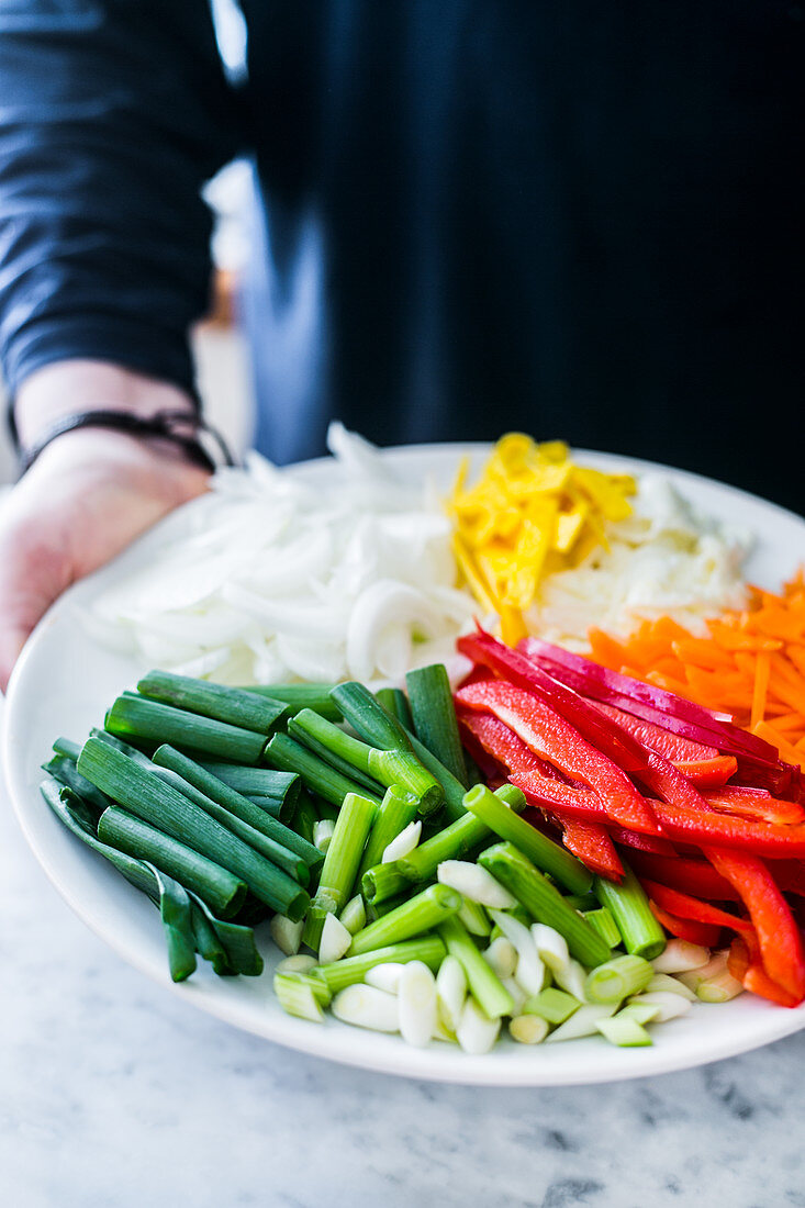 Hände halten Teller mit frisch geschnittenem Gemüse