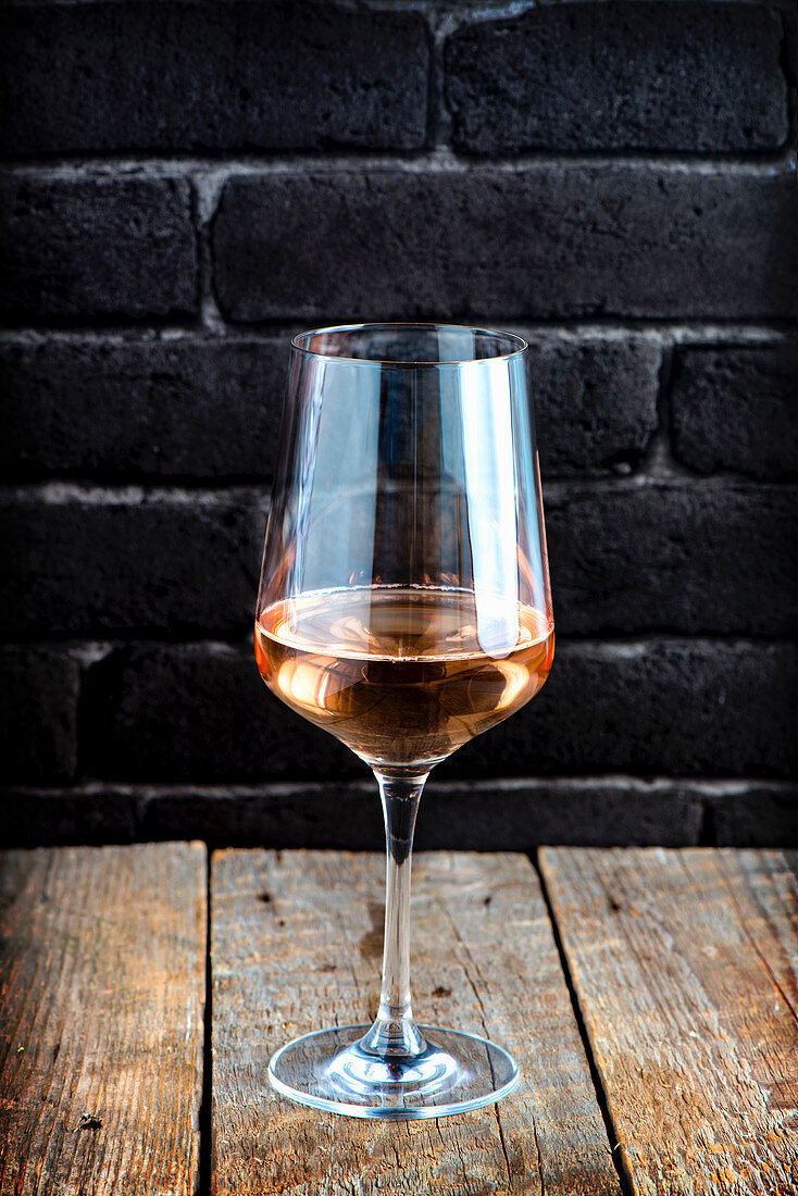 A single glass of rose wine on a rustic wood with black brick background