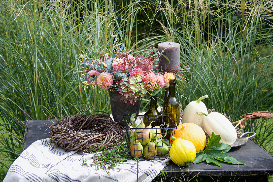 Herbst-Arrangement mit Kürbissen, Birnen und Gesteck auf dem Gartentisch
