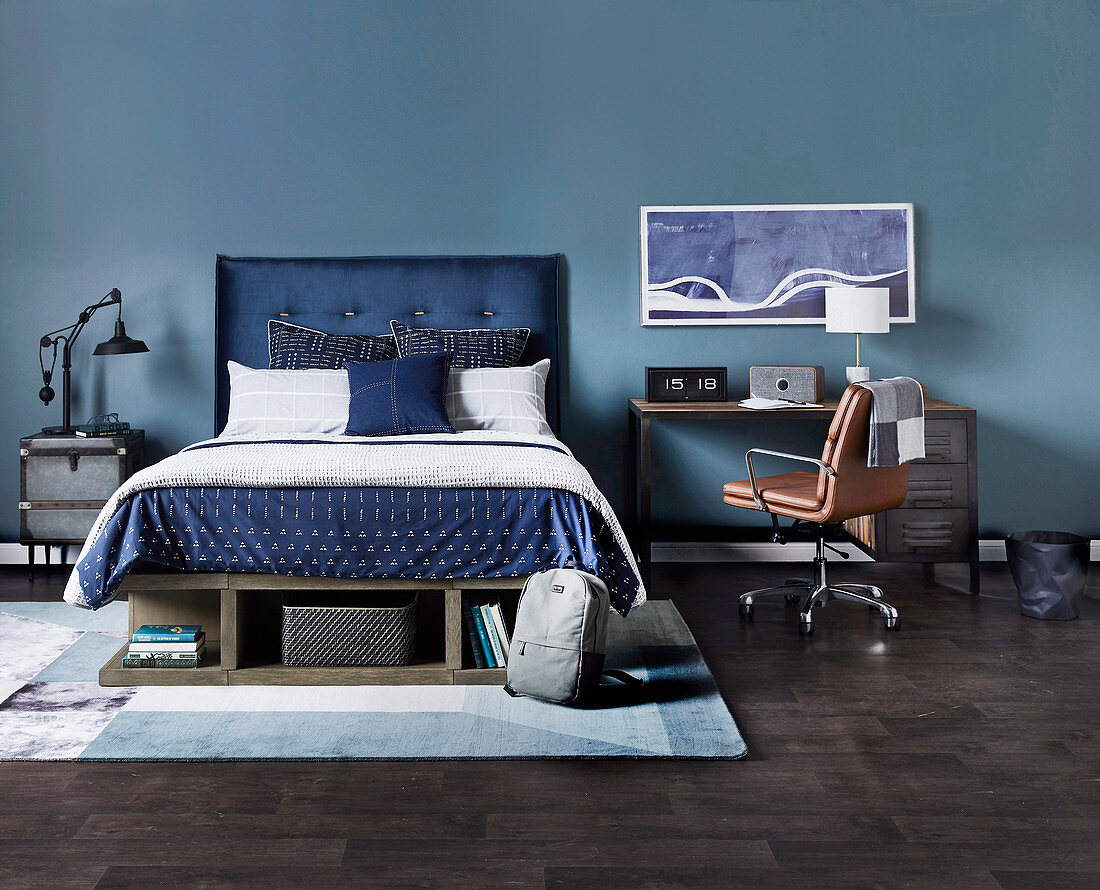 Double bed with blue headboard, next to desk with leather chair against blue wall