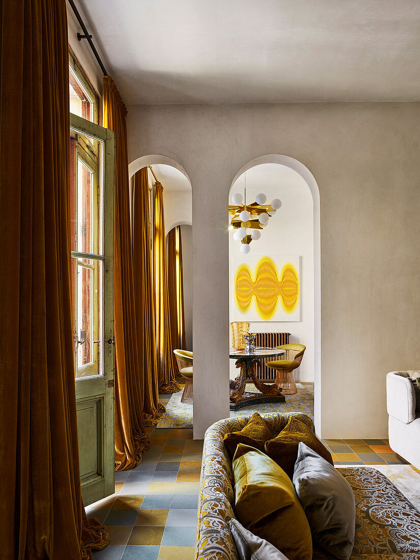 Elegantes Sofa mit Kissen vor Fenstertür mit bodenlangen Vorhängen im Wohnzimmer