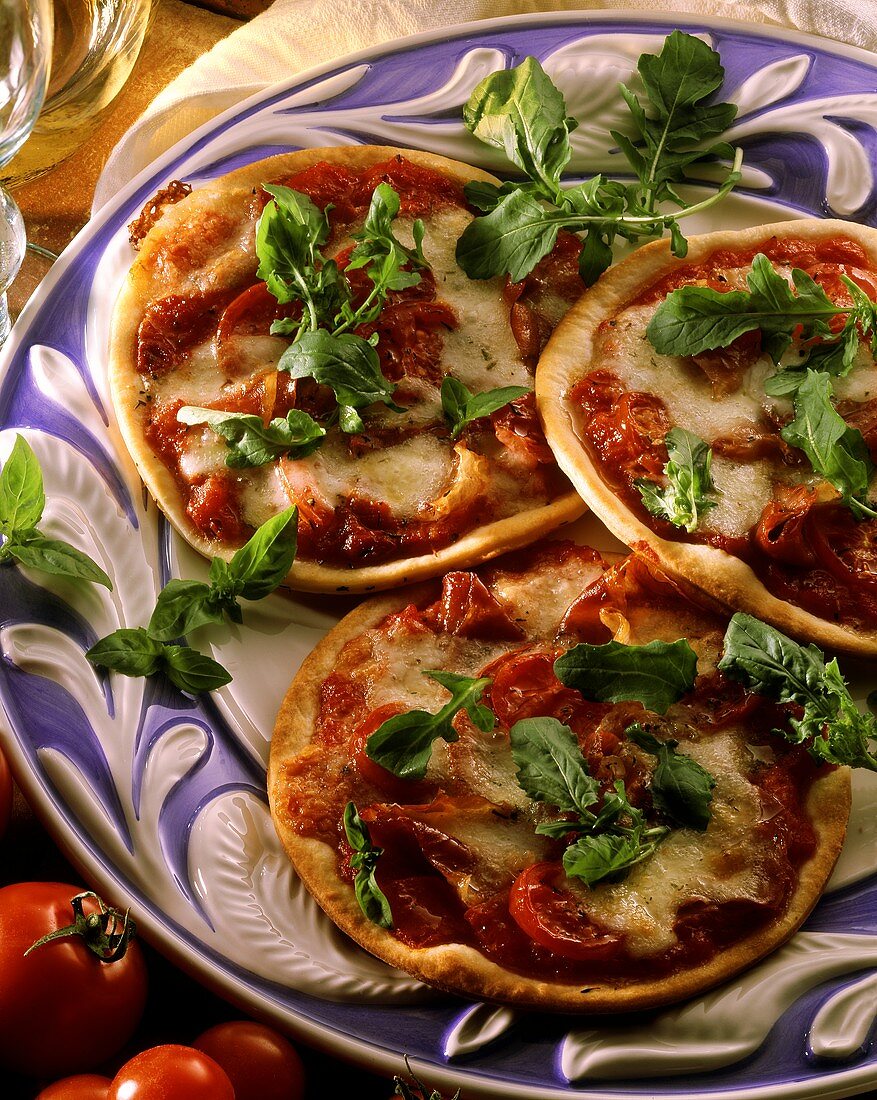 Three small pizzas with tomatoes, cheese and fresh rocket