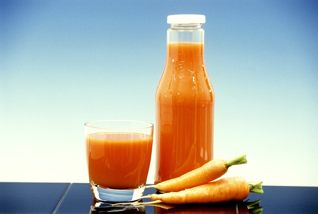 Carrot juice in glass and bottle with two fresh carrots