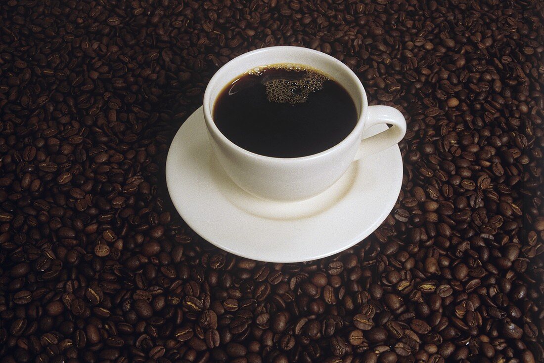 Kaffee in weisser Tasse auf Untergrund aus Kaffeebohnen