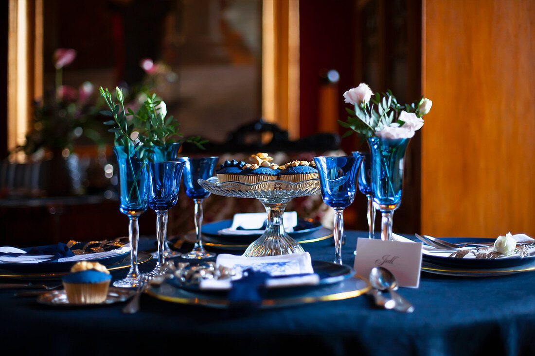 Blaue Gläser und Teller auf festlich gedecktem Tisch mit Blumen