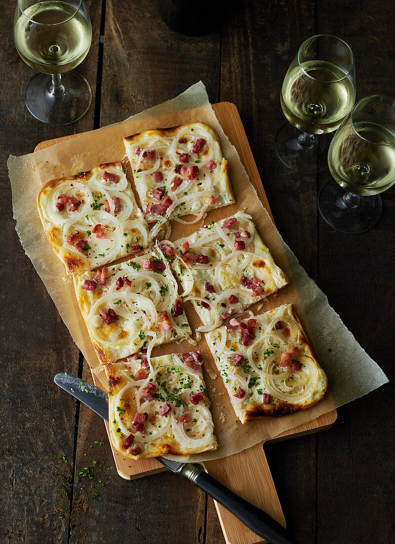 Tarte flambée with bacon and onions on a wooden board with three glasses of wine